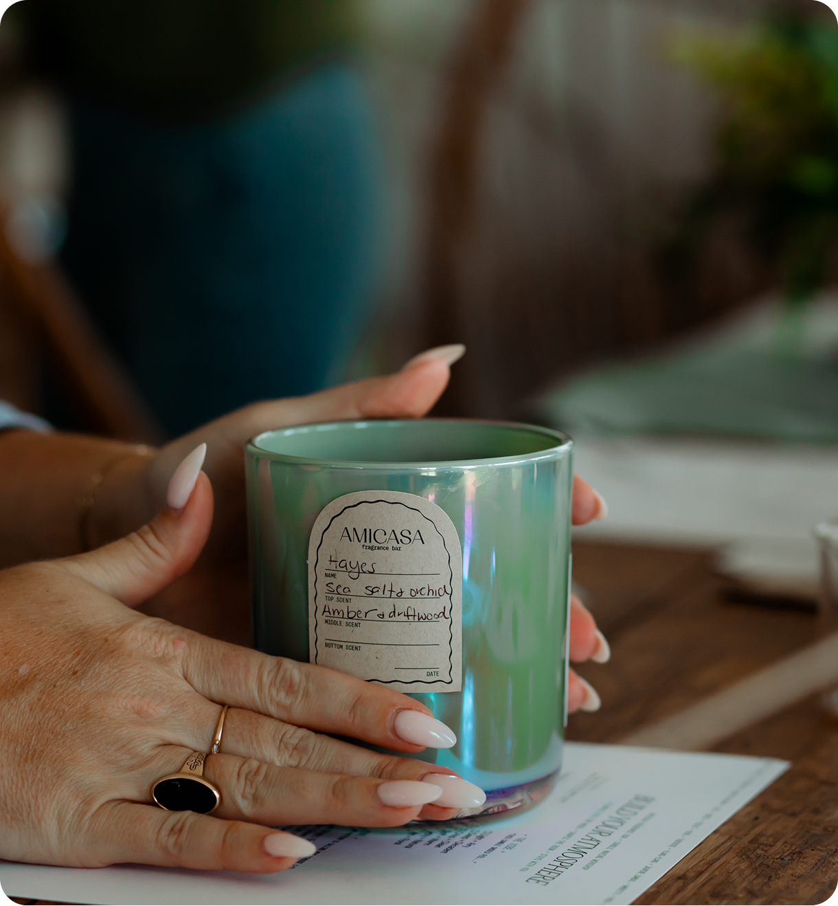 Person holding a green iridescent candle with a label on a blurred background