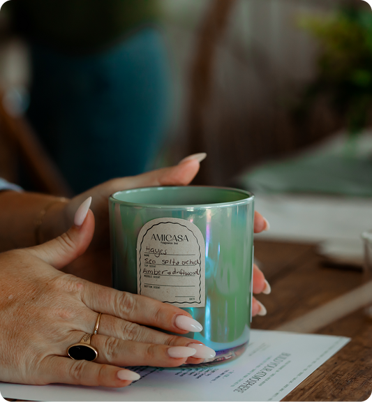 Person holding a green iridescent candle with a label on a blurred background